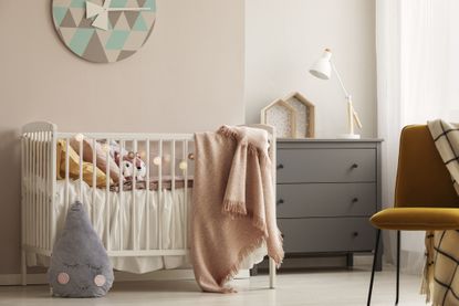 Best cot mattresses: Pillows and toy in white wooden crib with pastel pink blanket in bright nursery