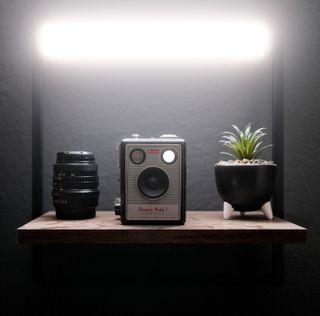 Aputure MT Pro tube light lighting a shelf with a lens, camera and plant on