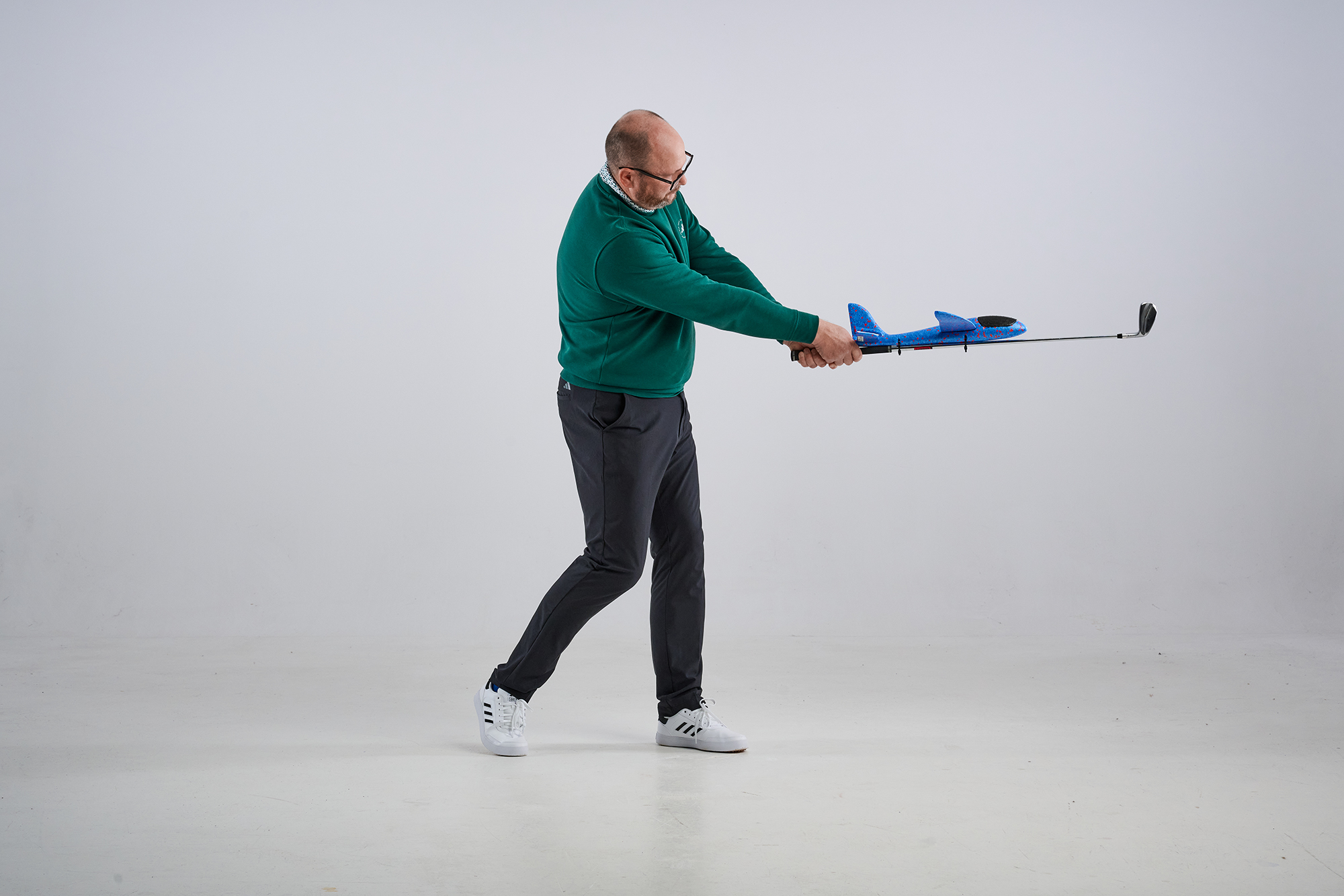 Russell Covey demonstrating an iron play drill using a toy plane, from side on with the plan attached to the shaft of the iron near the grip