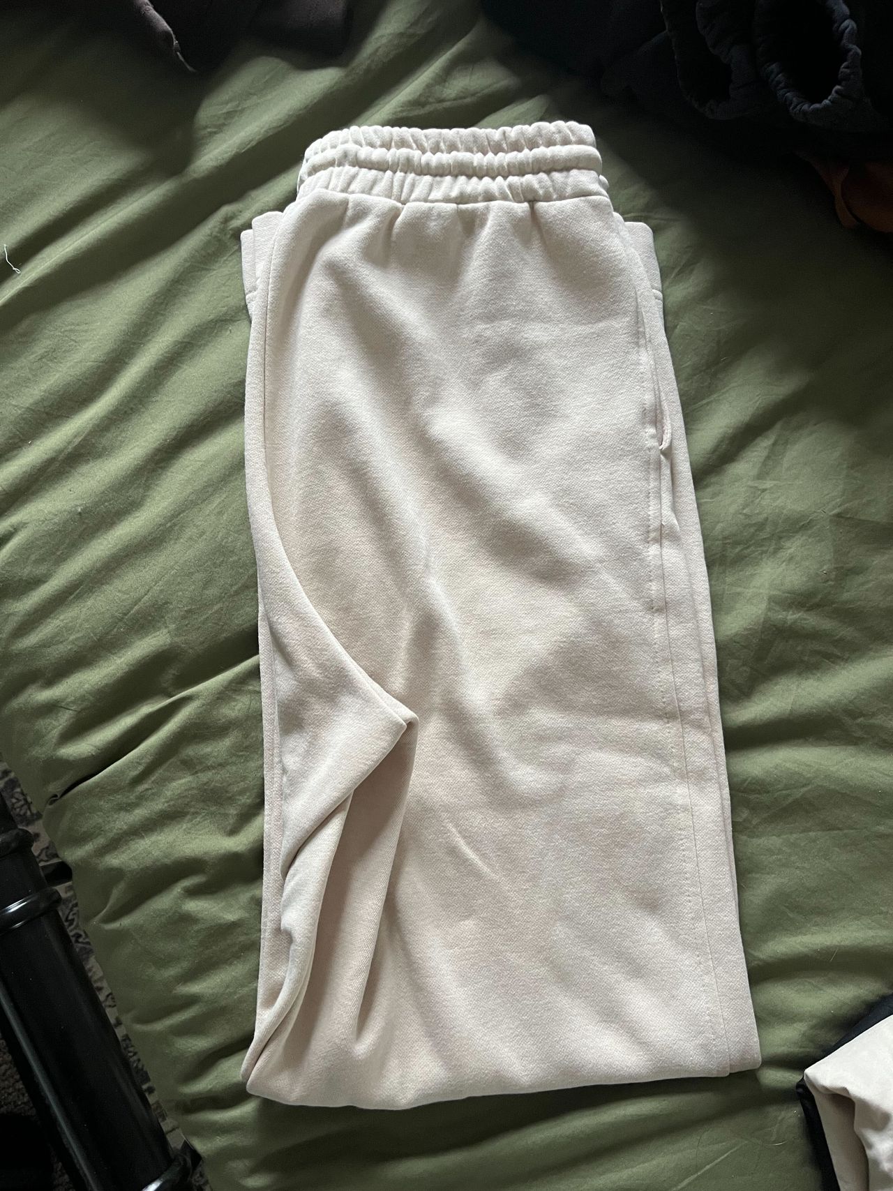 A pair of cream sweatpants folded in half on a green bed