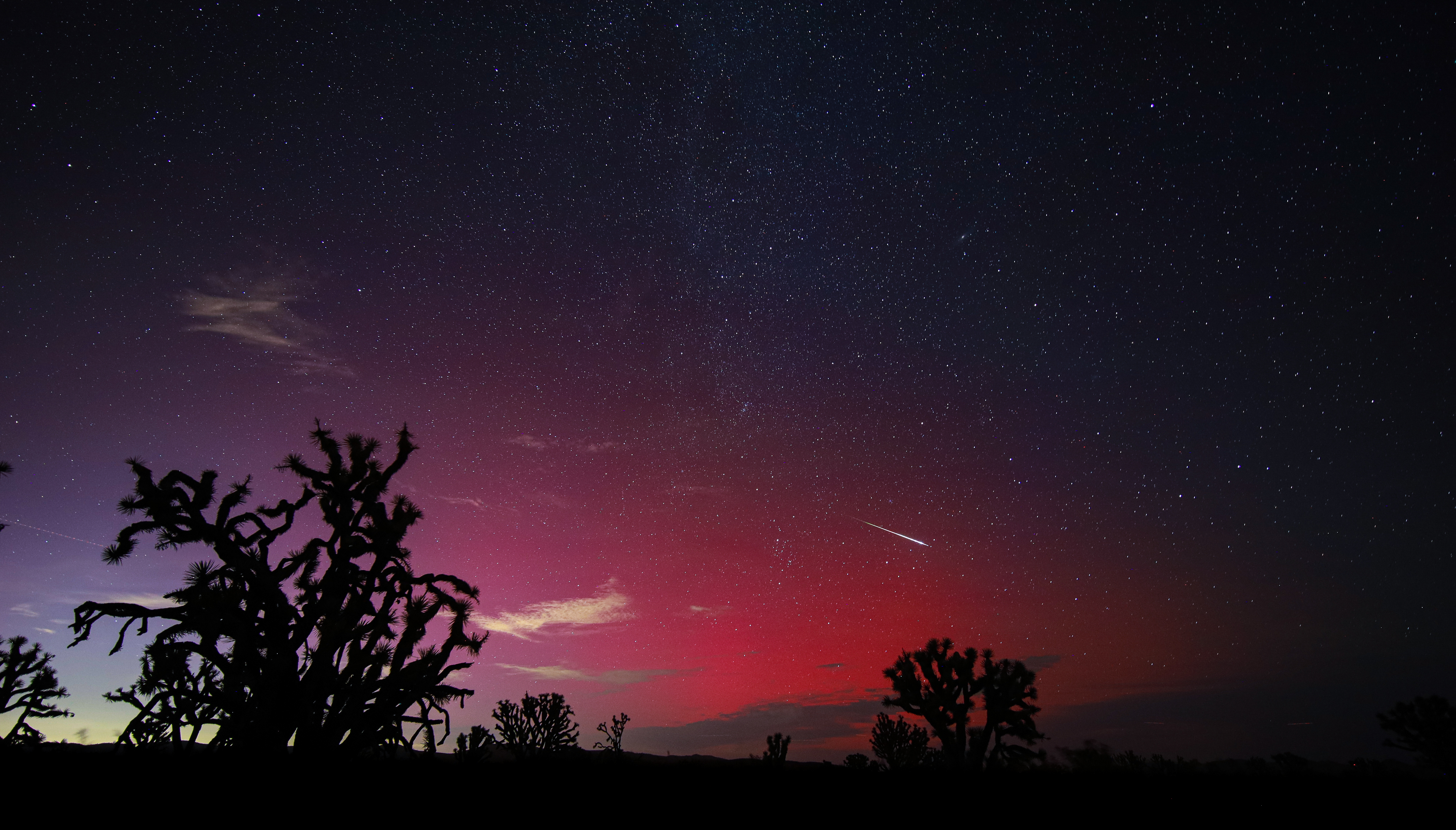 Bir meteorun uzun beyaz kuyruğu, aurora borealis tarafından koyu kırmızıya boyanan gökyüzü boyunca uzanıyor.