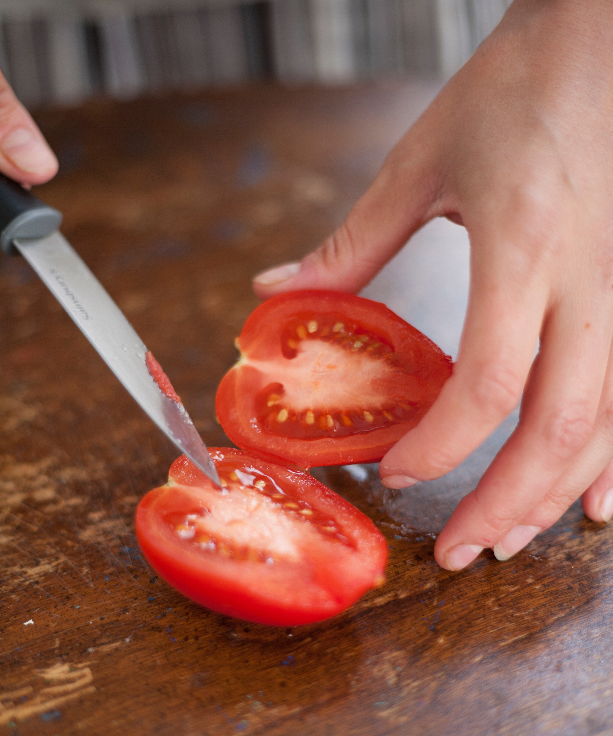 cutting a cherry plum tomato in half to extract the seeds