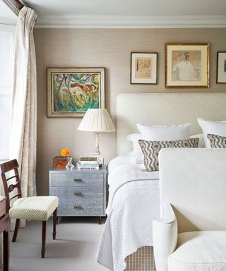 neutral bedroom with grasscloth wallpaper, silver bedside chest and artwork