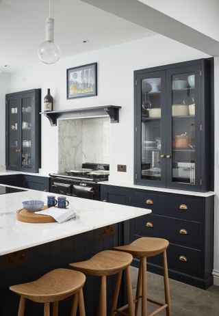 An example of how to make a small kitchen look bigger showing a kitchen with black cabinetry and white walls next to an island with wooden bar stools