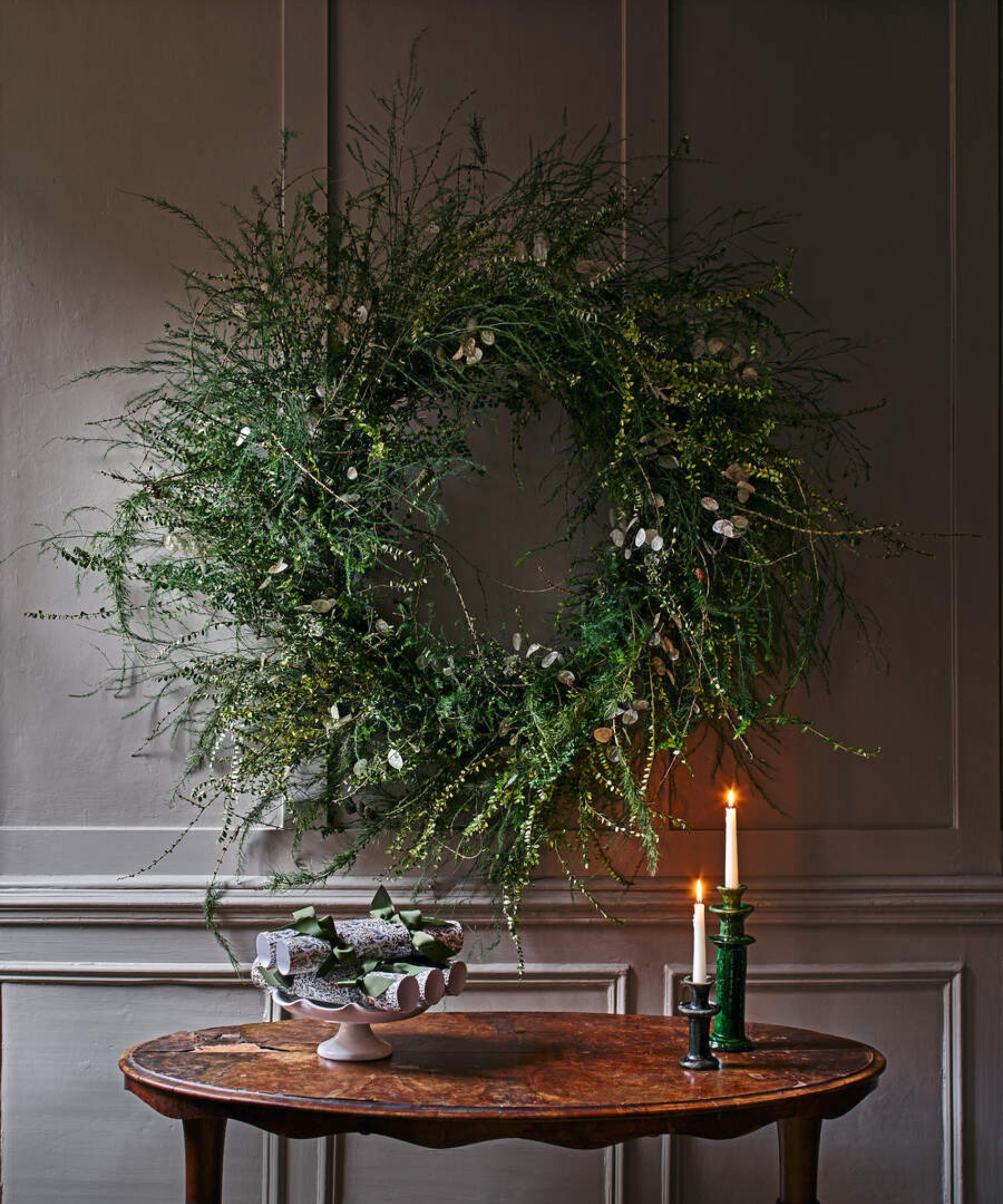 a whimsical Christmas wreath with stray branches hanging from the wall with a small table underneath with candles and a small decorative tray