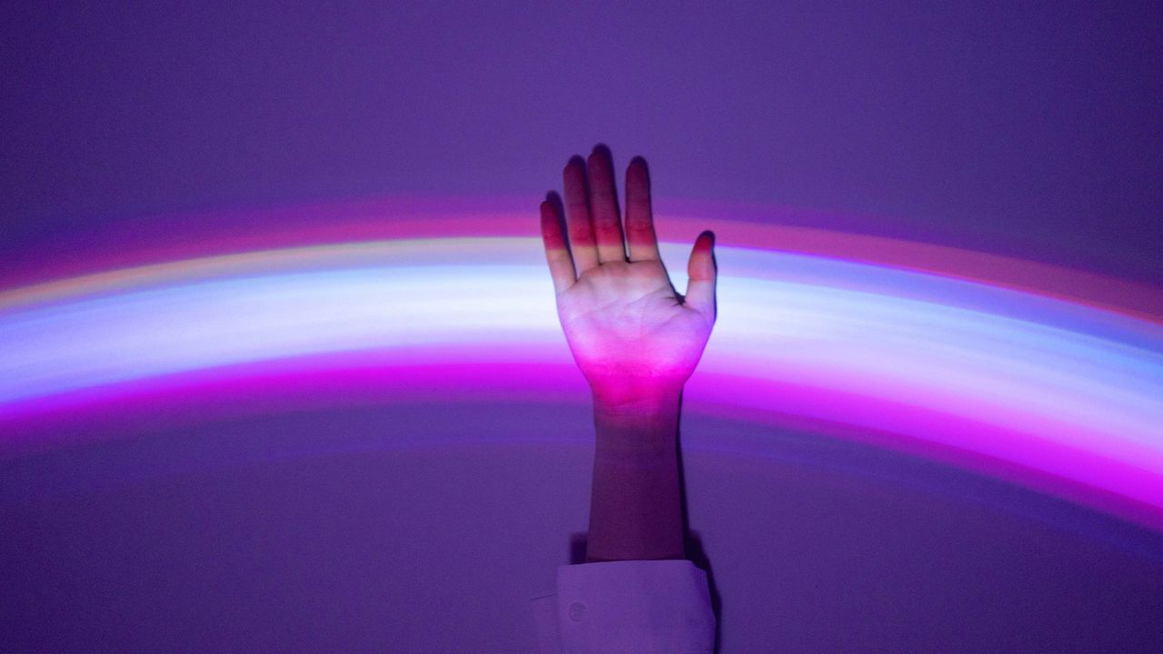 A rainbow is projected upon a hand reaching up into the light.