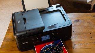 The Canon PIXMA TR7650 inkjet 4-in-1 printer in use with an A4 color print coming out of its front tray