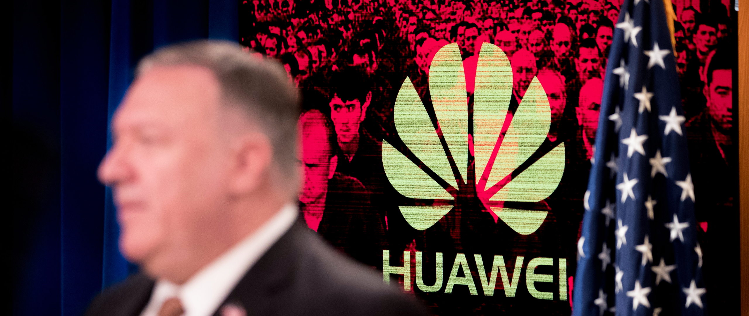A monitor displays the logo for Huawei behind Mike Pompeo