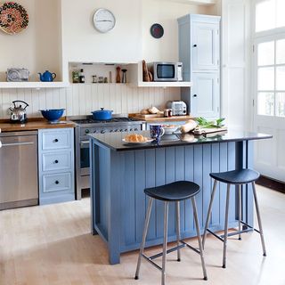 dark blue island, wooden flooring, stainless steel oven and white walls