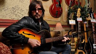 Rival Sons guitarist Scott Holiday holds a vintage acoustic guitar as he poses in a guitar shop