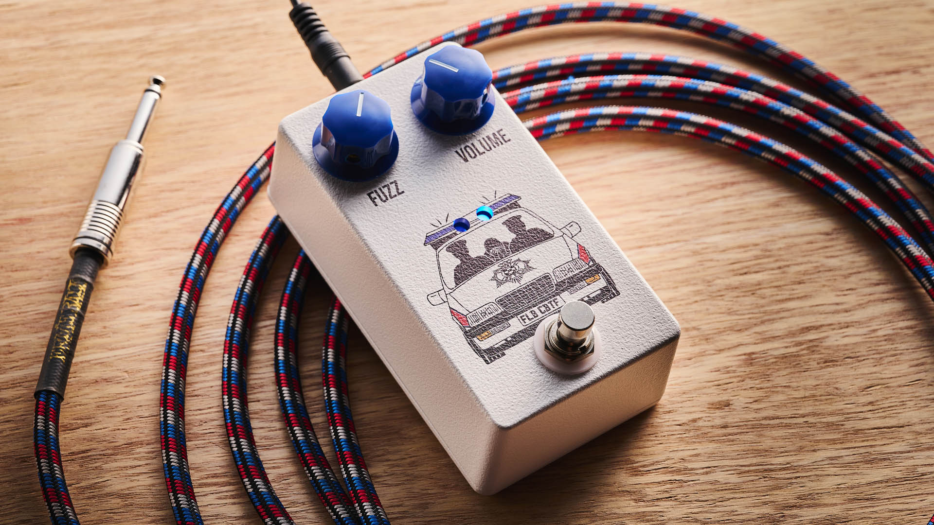 Funny Little Boxes Caught By The Fuzz: inspired by Supergrass, this two-knob fuzz has a white enclosure, blue dials, and a comic graphic of someone being apprehended in a police car.