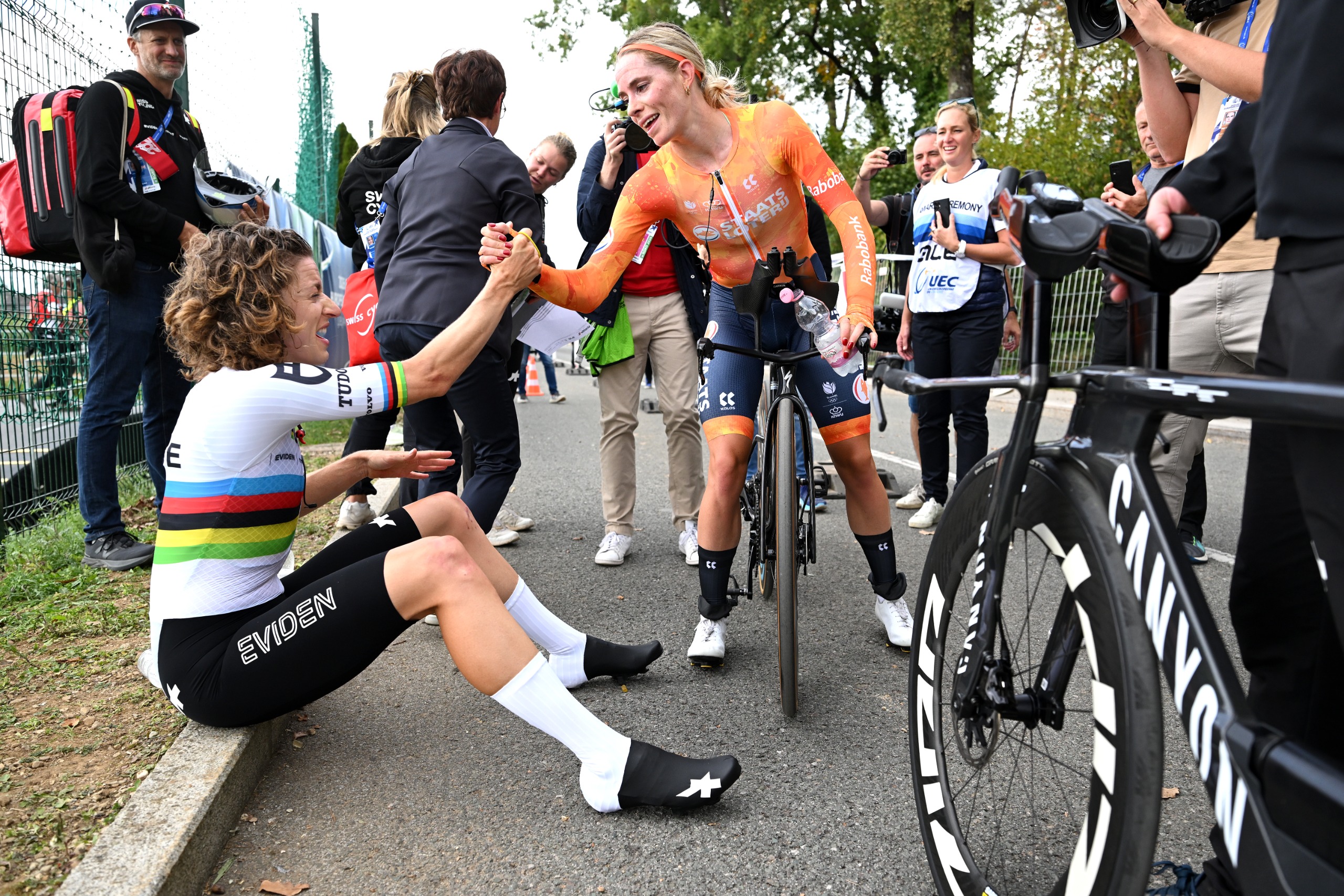 Dutch rider Demi Vollering leans off her bike to congratulate world champion Marlen Reusser, who is sat on the kerb, after the race