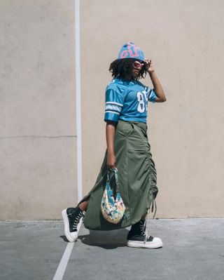 influencer wears olive green skirt, light blue jersey, and platform converse in front of a concrete wall