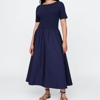 A model wearing a navy blue midi short-sleeve dress with sandals shot against a white background