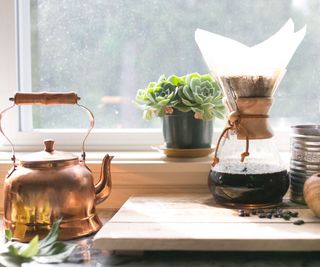 drip coffee maker on a windowsill with a copper kettle