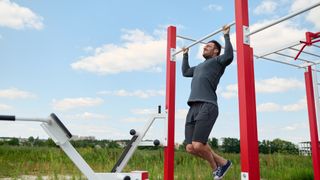 Man performs pull-up exercise outdoors