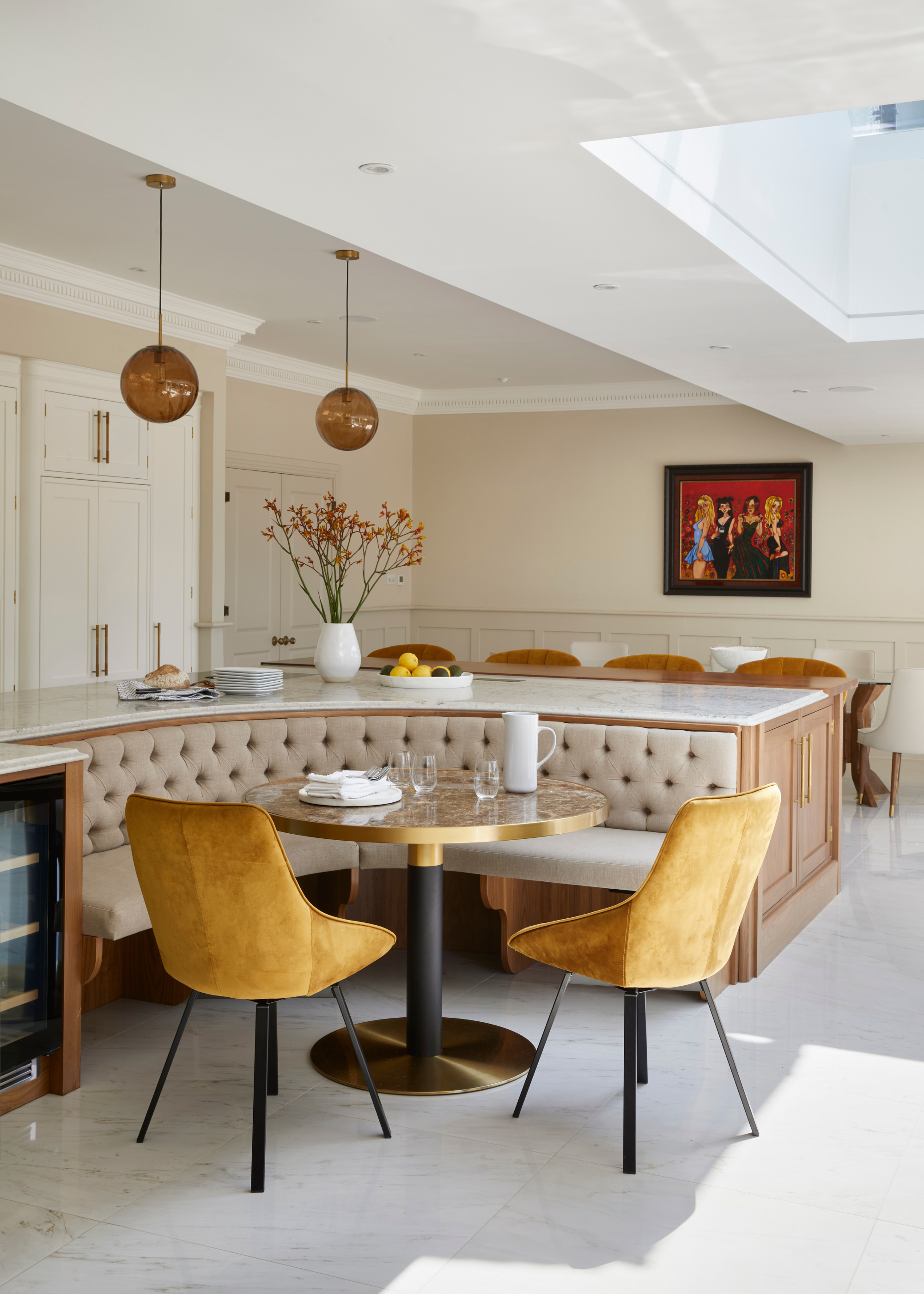 A light kitchen diner with curved banquette seating built into one side of the island, a table in front and a couple of mustard yellow chairs on the opposite side