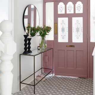 Pink door with frosted glass opening next to steel and glass hallway stand with a glass vase with pink flowers in front of mirror
