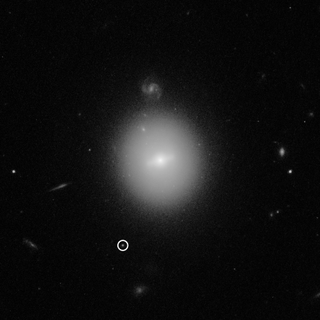 This Hubble Space Telescope image shows the location of an intermediate-mass black hole named 3XMM J215022.4−055108 (in the white circle). Hubble's high-resolution imagery revealed that the black hole resides inside a dense star cluster far beyond the Milky Way galaxy, in the outskirts of another galaxy pictured at the center of this image.