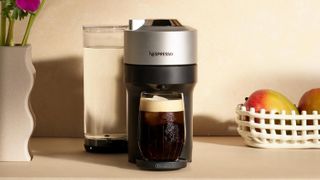 En svart och silvrig Nespresso Vertuo Pop+ står på en köksbänk och har precis bryggt en kopp kaffe.