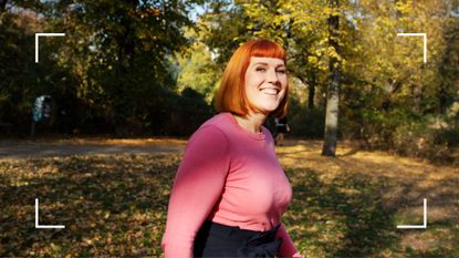 Woman standing alone smiling in a forest facing the camera, wearing workout clothes after weighing up walking vs running