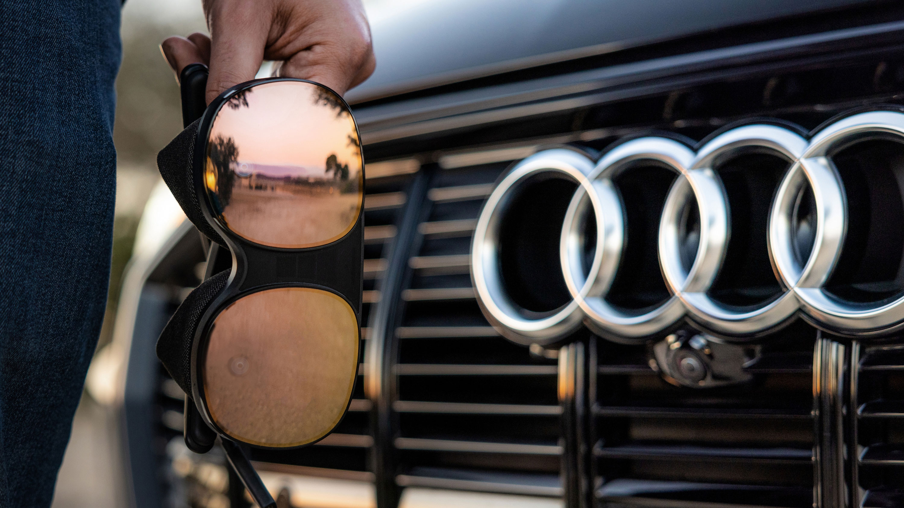Hand holding VR headset in front of Audi badge on a car
