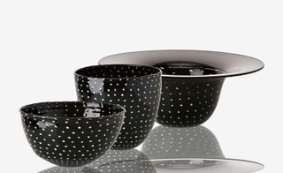 Three black white spotted bowls of different sizes on a reflective surface.