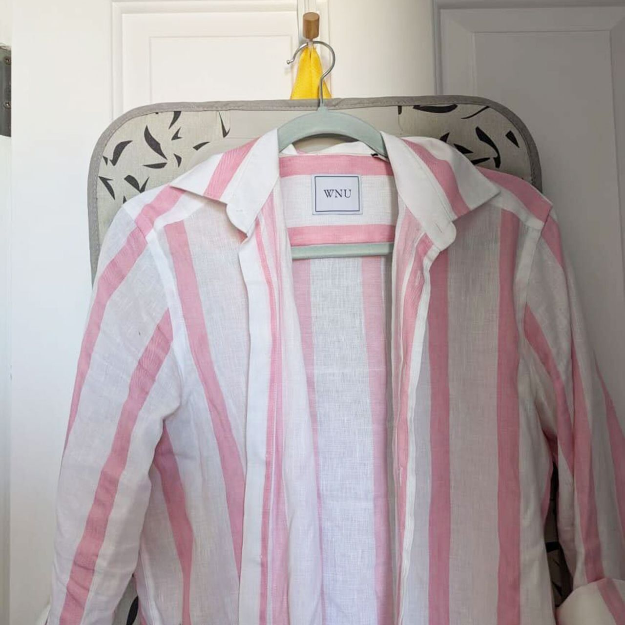 Pink and white striped shirt hanging in front of ironing mat