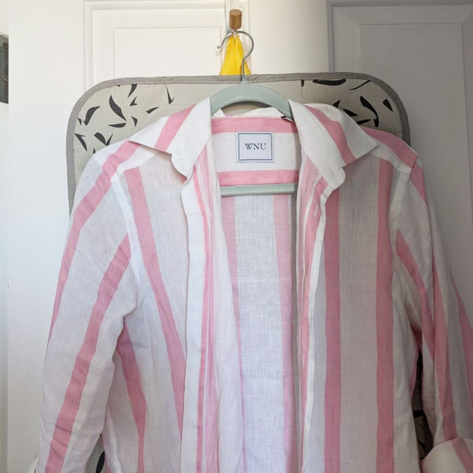 Pink and white striped shirt hanging in front of ironing mat