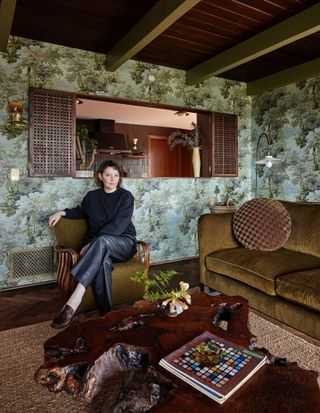 Jamie Haller sits in a house wearing a boatneck sweater and her shoes