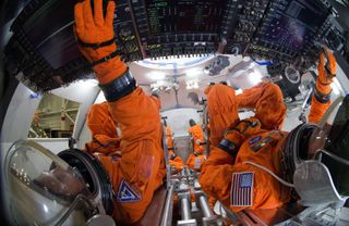 overhead view of spacesuited engineers in a spacecraft reaching for panels
