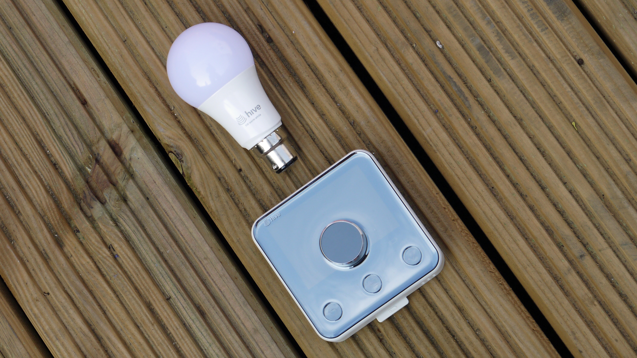 The Hive Thermostat on wooden decking with a Hive smart light bulb above it