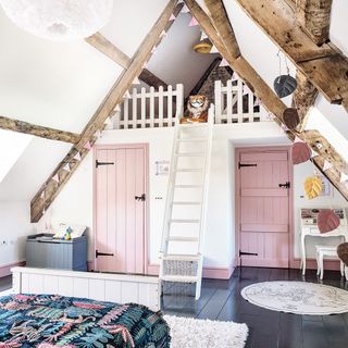 child's bedroom loft conversion with dark floor white walls and two pink doors with ladder to cubby hole in exposed beams with toy tiger