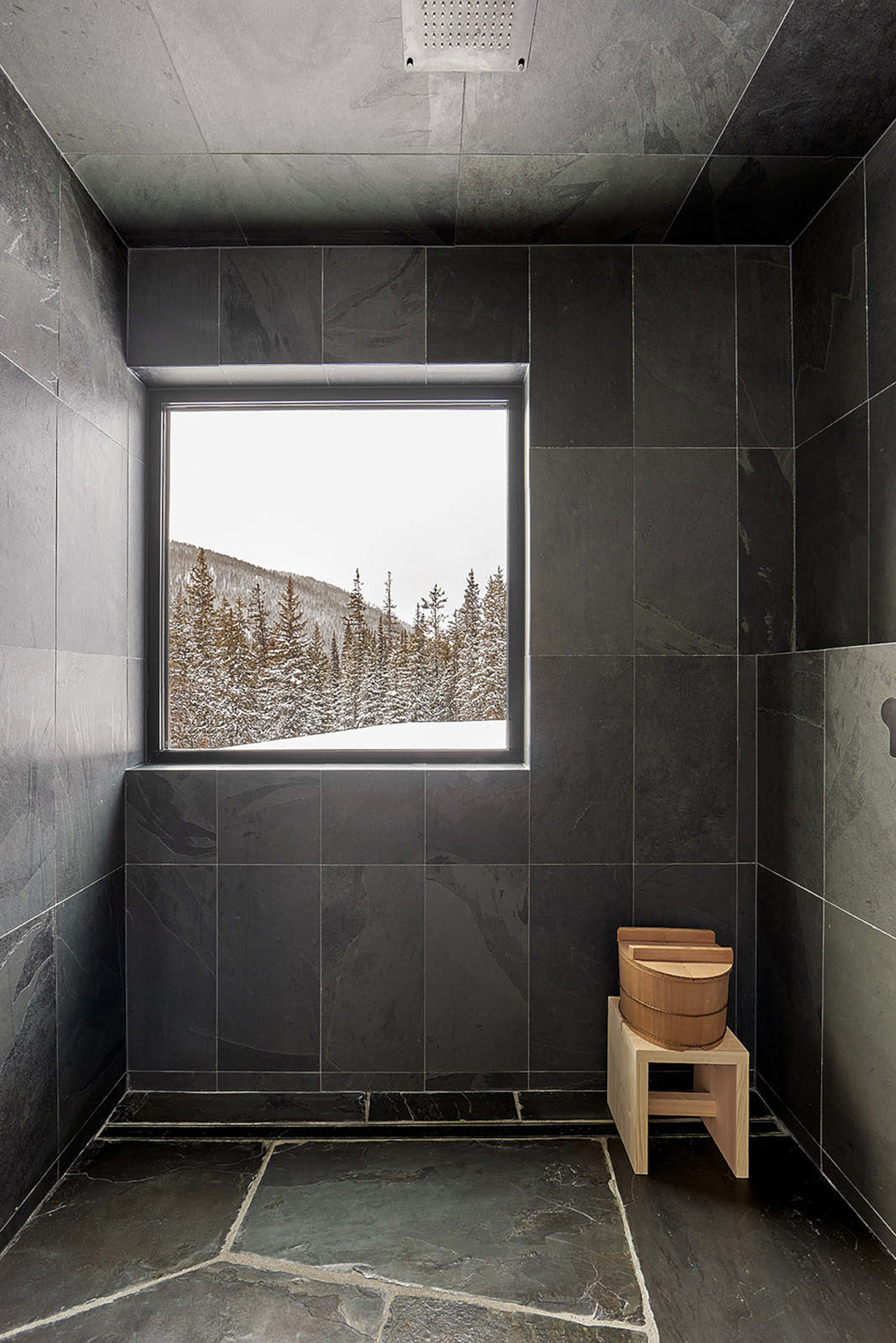 A bathroom with wall-to-ceiling dark grey tiles and a light wood stool