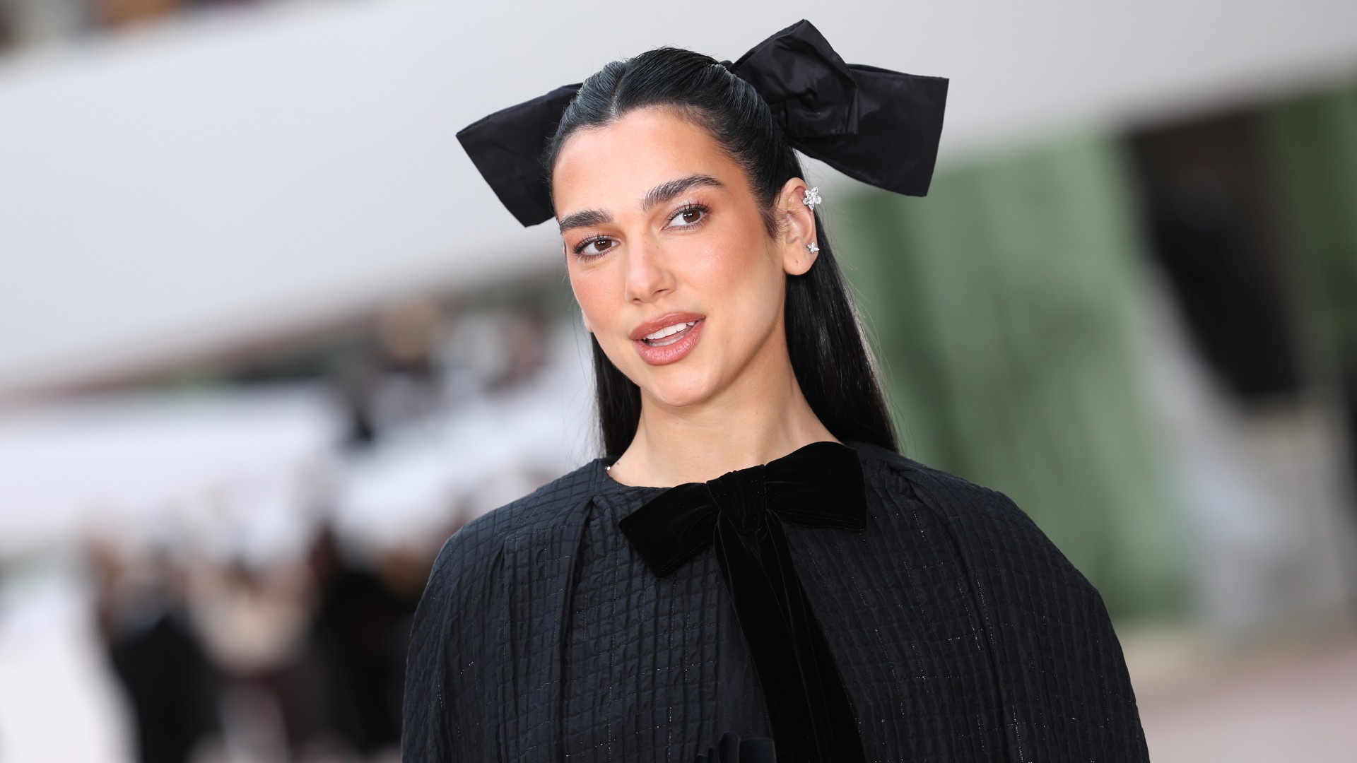 dua lipa wearing all black with a large black hair bow