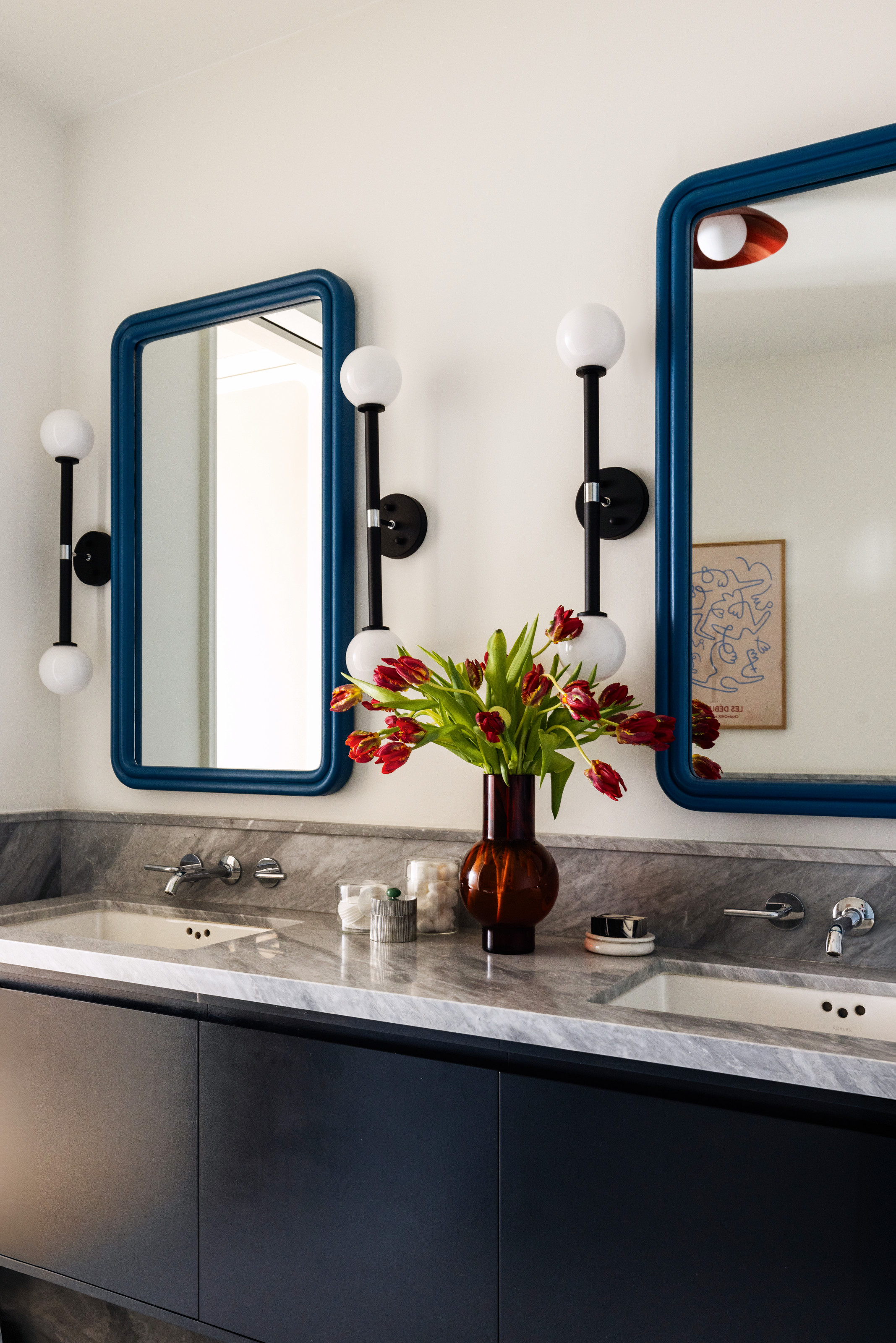 Bathroom with black vanity with grey stone countertop and in-built sinks, chunky blue rectangular mirrors and black globe dual wall lights