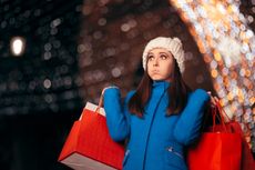 A woman holds shopping bags while looking flustered.