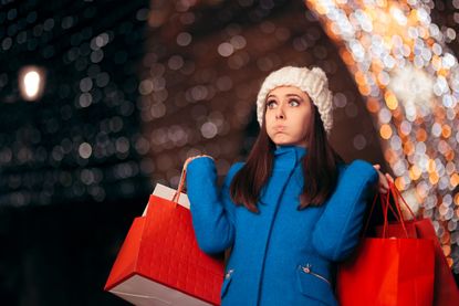 A woman holds shopping bags while looking flustered.