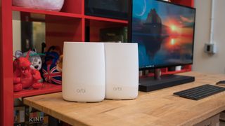 Two Netgear Orbi Mesh WiFi network routers sitting on a desk near a computer monitor
