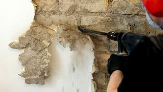 Person using asn SDS drill to remove plaster from a wall