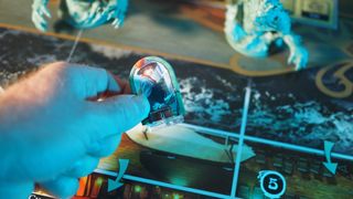 A hand placing a token of a woman onto a sea-themed board