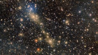 Thousands of stars of different shades of gold and white sparkle in the darkness of space, with a streak of gold going through them