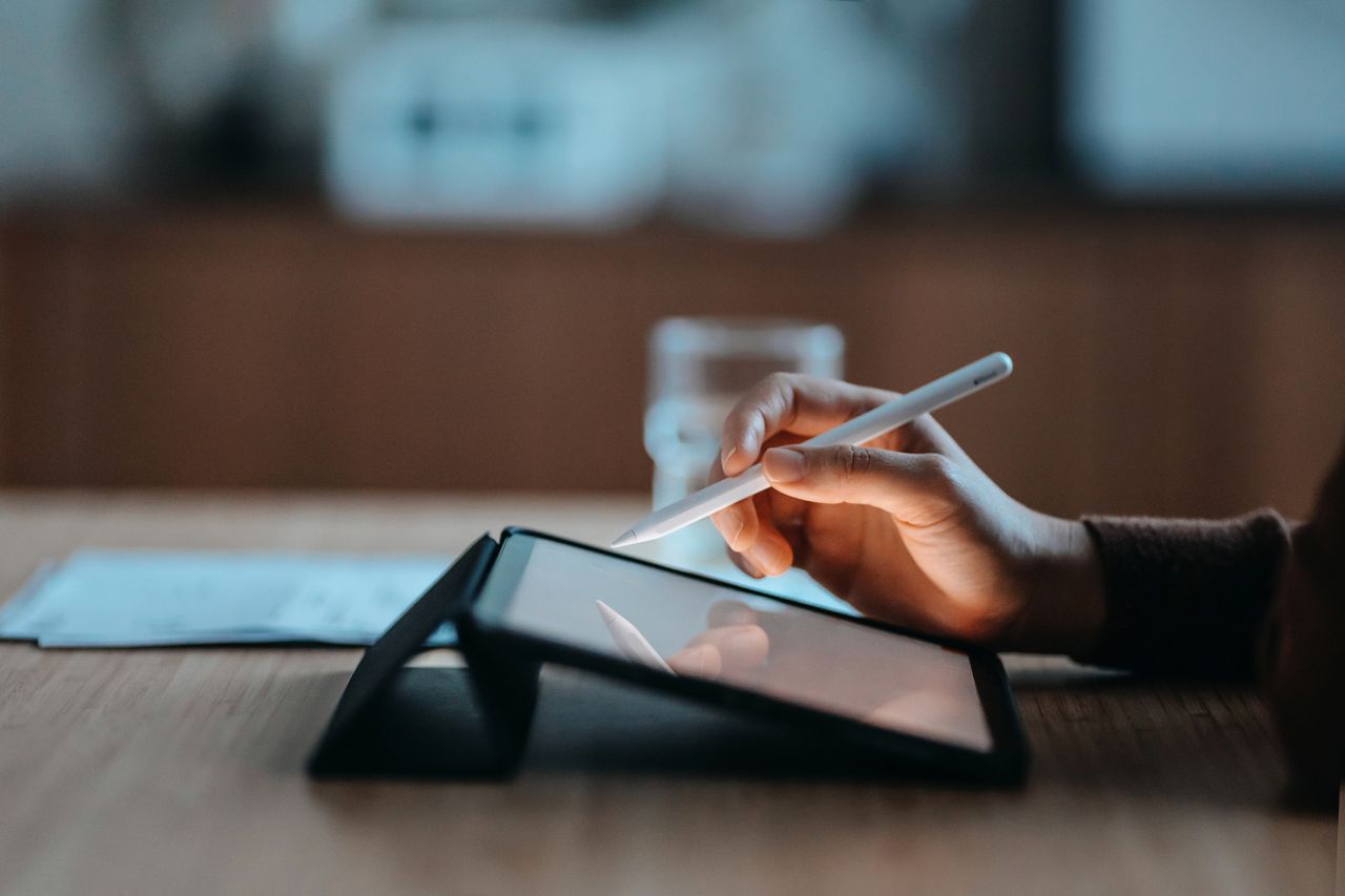 Side view, close up of a female hand using digital tablet with a pen while working from home. Lifestyle and technology