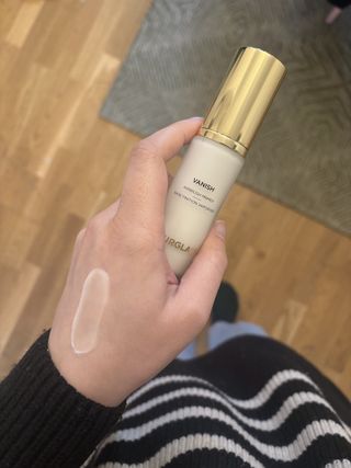 Mica Ricketts holding Hourglass Vanish Airbrush Primer with swatch of product on back of hand