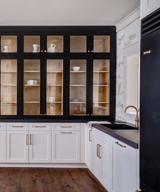 black and white kitchen with white cabinets, black painted glazed upper cabinet and black countertops, hardwood floor, brass faucet and hardware,