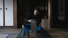 A craftsman on a tatami mat carving a bamboo whisk