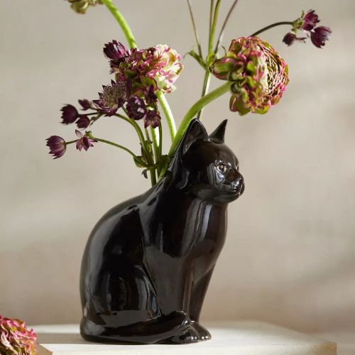 Black ceramic vase in the shape of a cat, holding purple and pink blooms