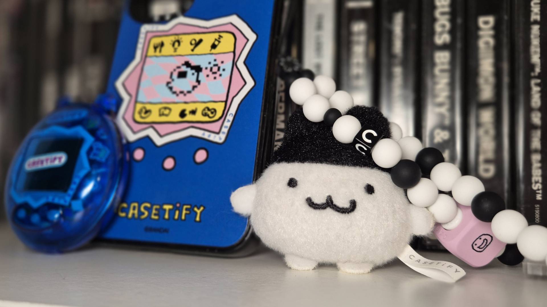 Photo of the Casetify Tamagotchi accessories sitting in front of a row of PlayStation games.