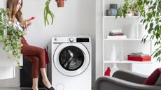 woman in white and red sat next to an AO washing machine