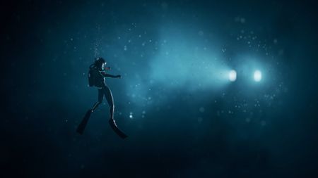 A lone diver caught in the headlights of an underwater machine during the Subnautica 2 trailer. 